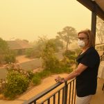 A woman, on a balcony, wears a face mask to protect herself against very dangerous level of air pollution.  A thick yellow fog coming from the nearby forest fires covers Canberra city.